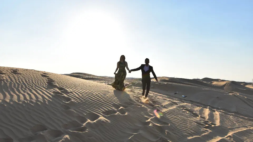 Vom Chat auf Dating Seiten zum ersten Treffen: ein Paar geht Hand in Hand über eine Sanddüne in der Sonne