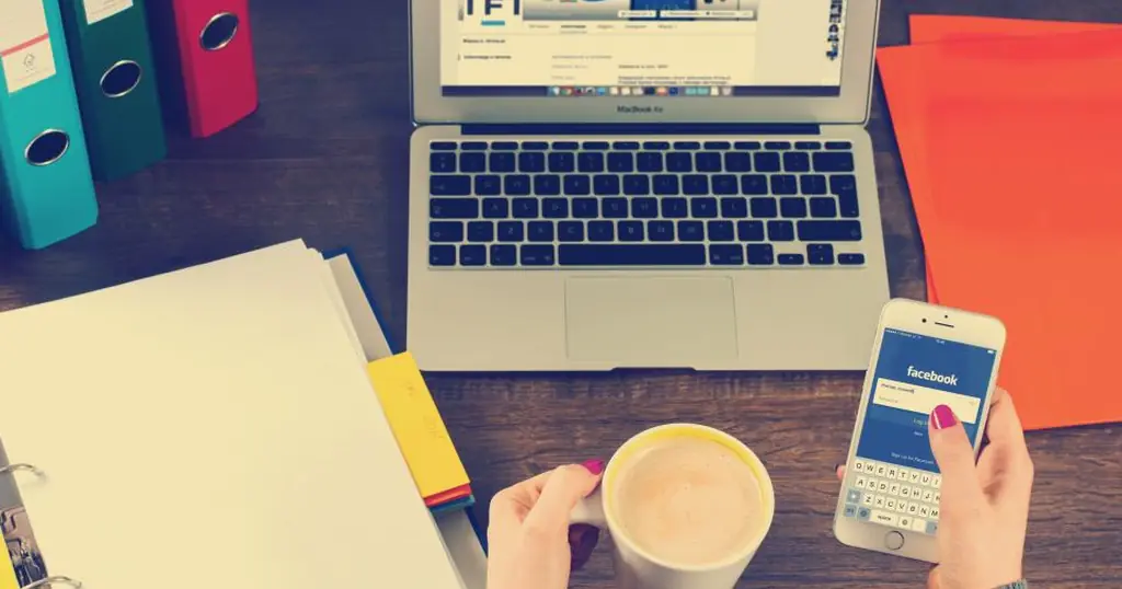 Online Dating: Hände mit Smartphone und Kaffee vor einem Laptop auf dem Schreibtisch
