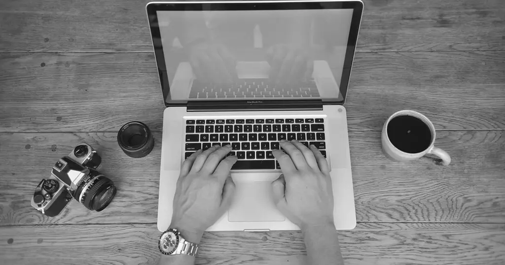 Love Scam erkennen: Hände auf der Tastatur eines Laptops, daneben eine Kamera