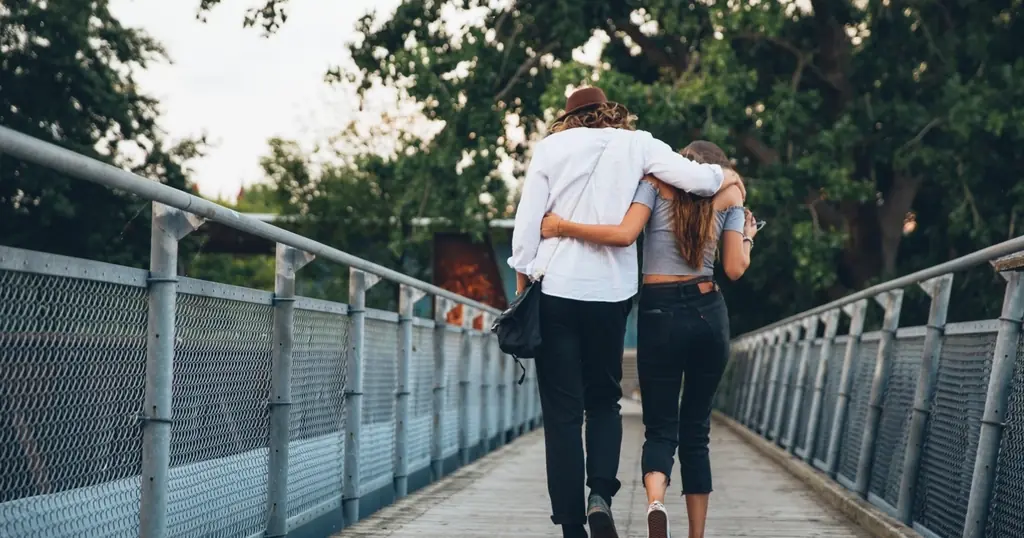 Dating Seiten: ein Paar geht Arm in Arm über eine Fußgängerbrücke im Grünen